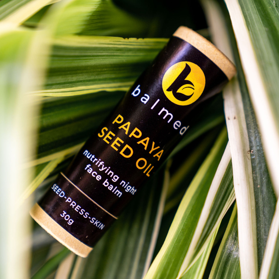 Stick of Papaya Seed Oil night balm lying on green leaves