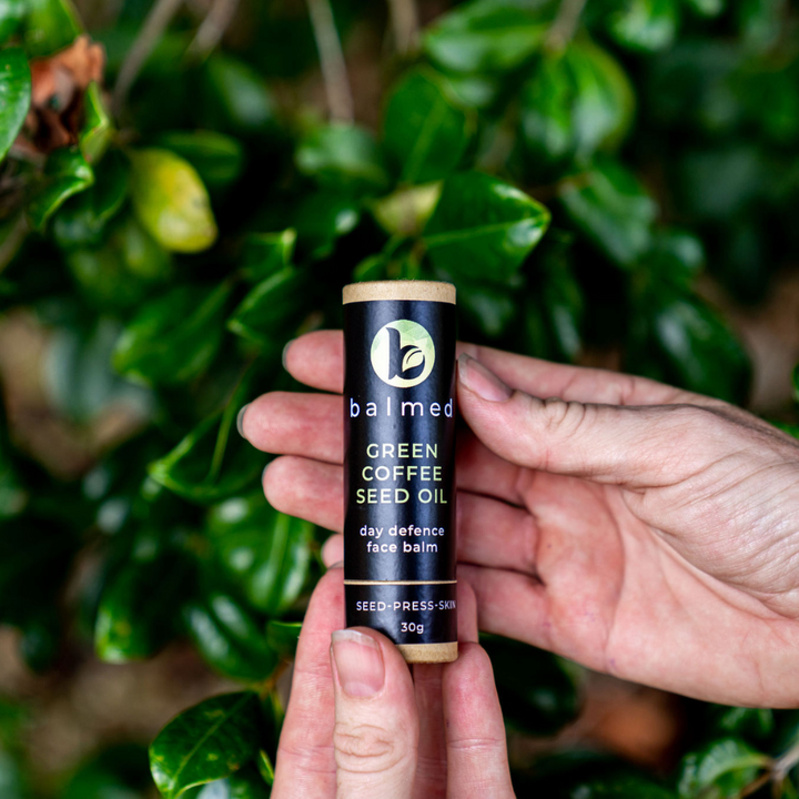 A hand holding a single stick of green coffee seed oil face balm