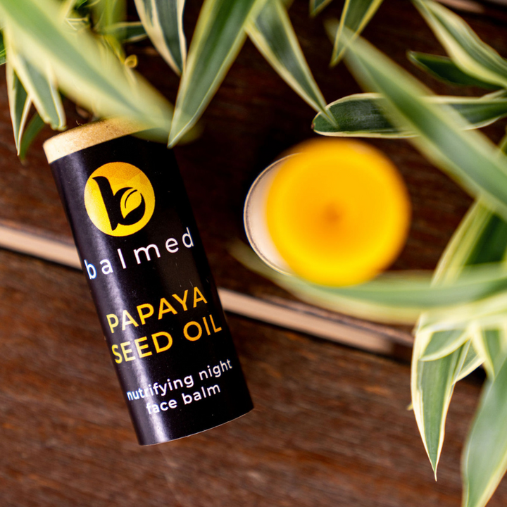Stick of Night face balm on a wooden bench. The lid of the balm is off and the product is slightly out of focus.